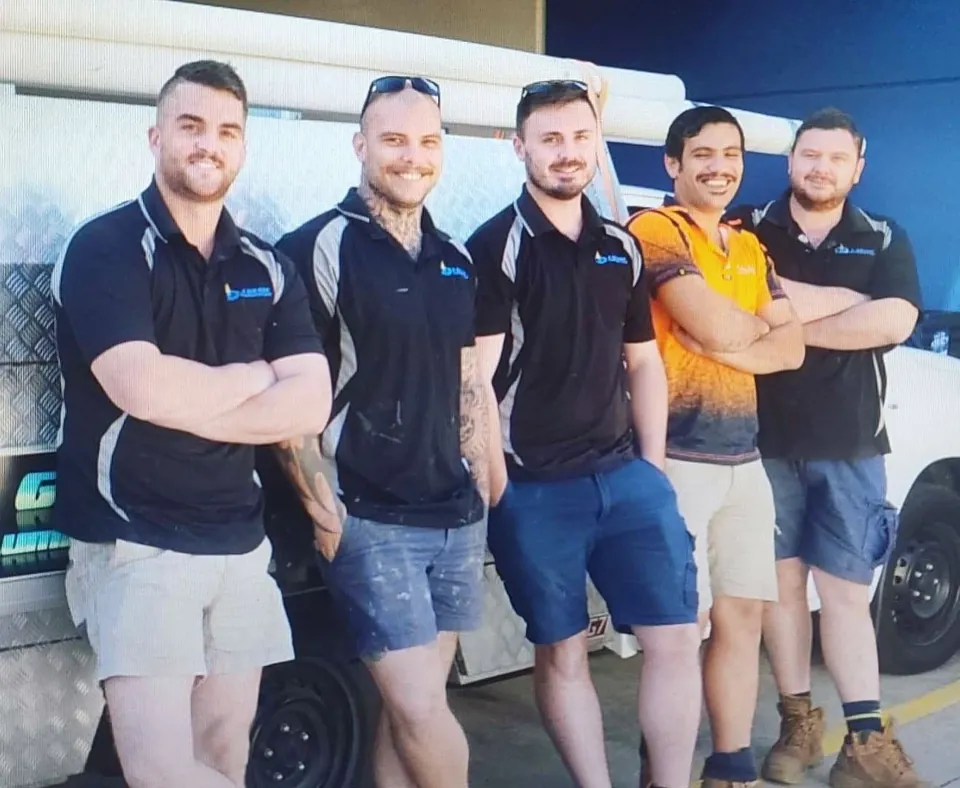 Five A Grade Plumbing and Gas team members standing with arms crossed in front of a branded backdrop
