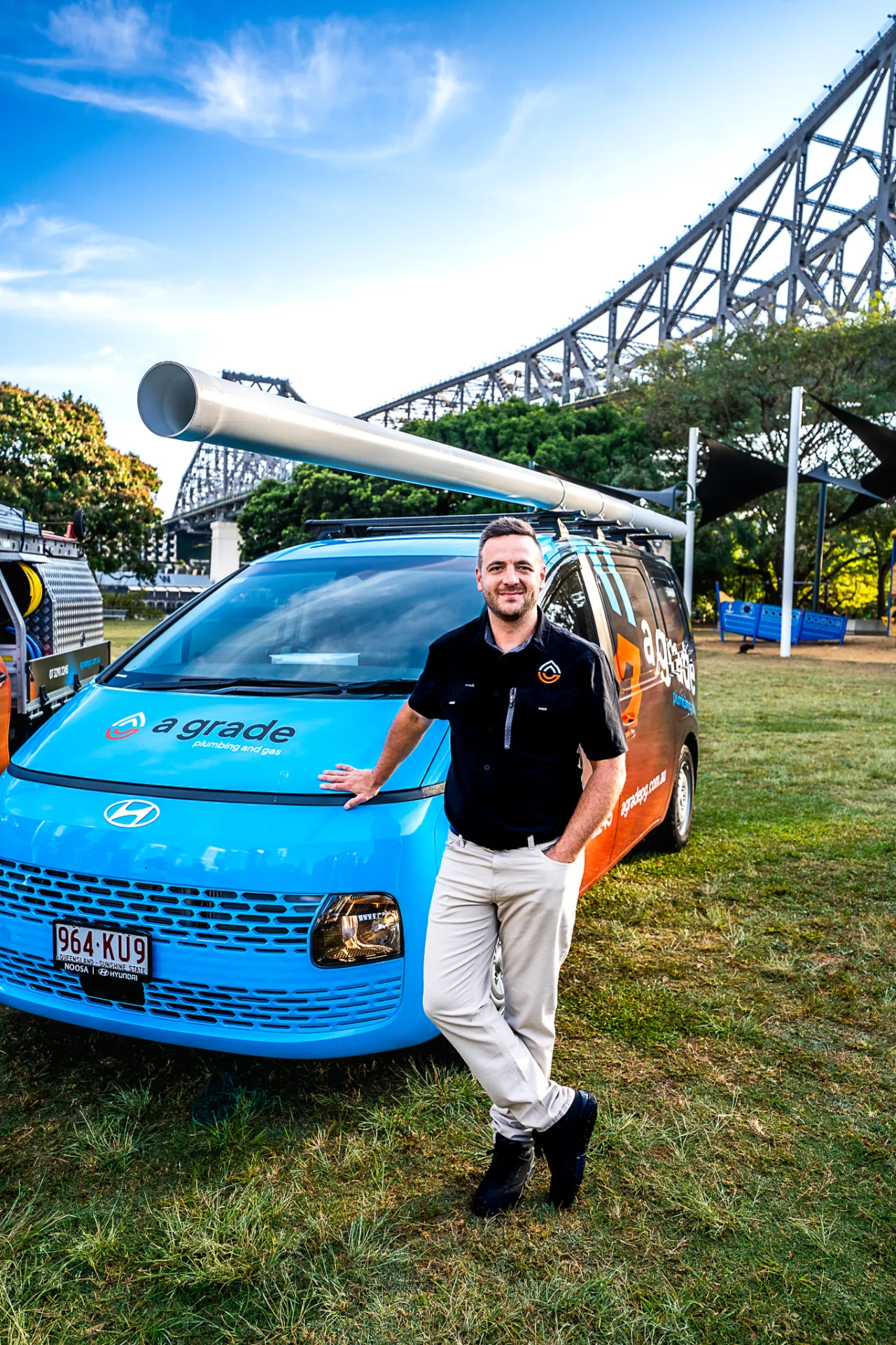 A Grade Plumbing and Gas Brisbane plumber leaning on a branded van in front of the Story Bridge